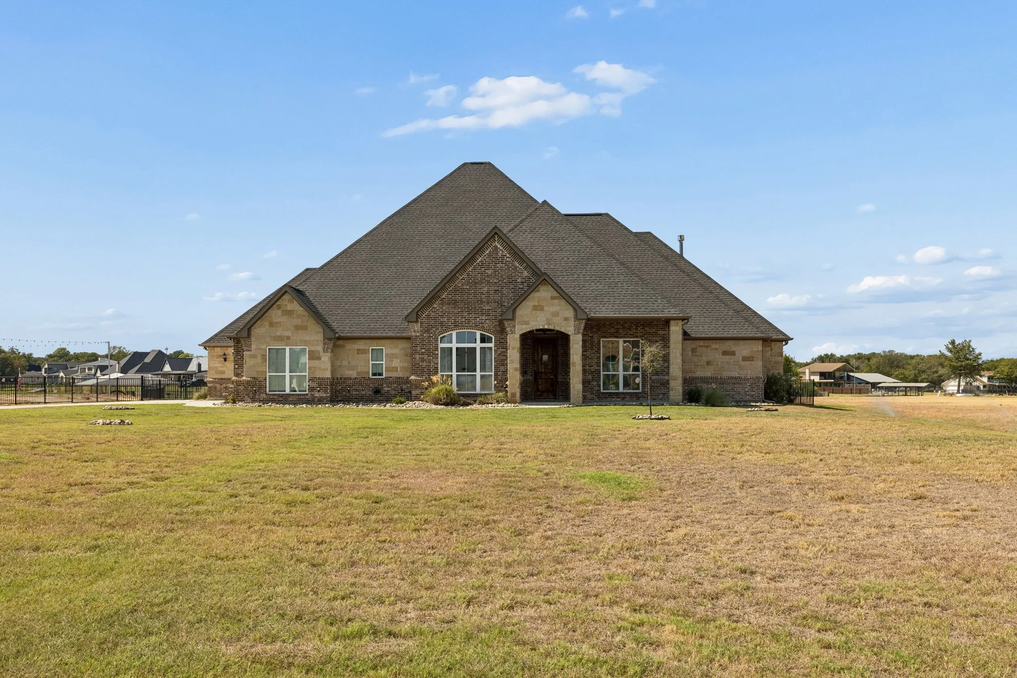 Brick and stone facade, arched entryway, gabled roofline, multiple window styles, expansive lawn