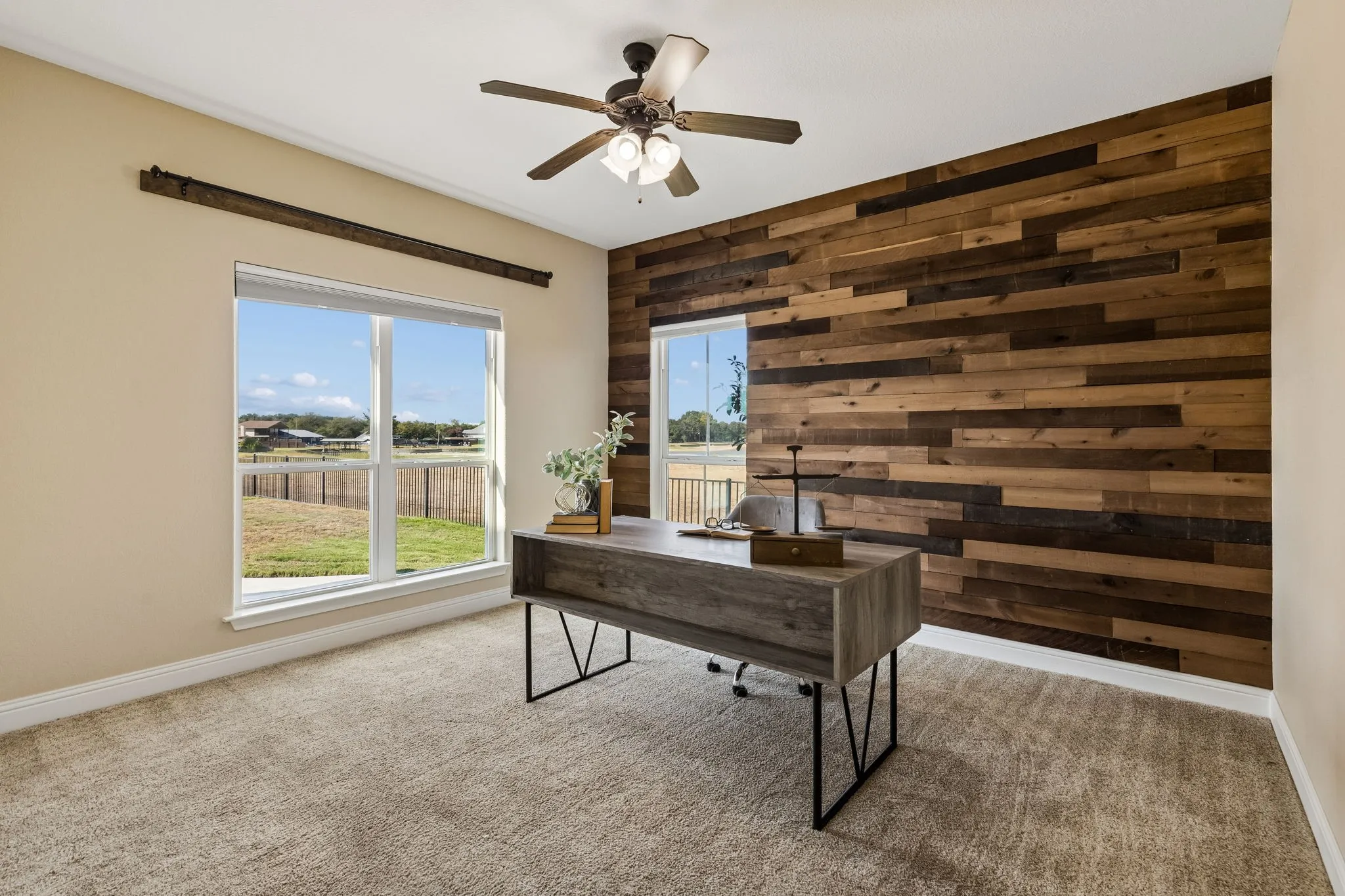 Accent wall featuring wood-finish paneling, ceiling fan with integrated lighting, two double-hung windows, and carpeted flooring