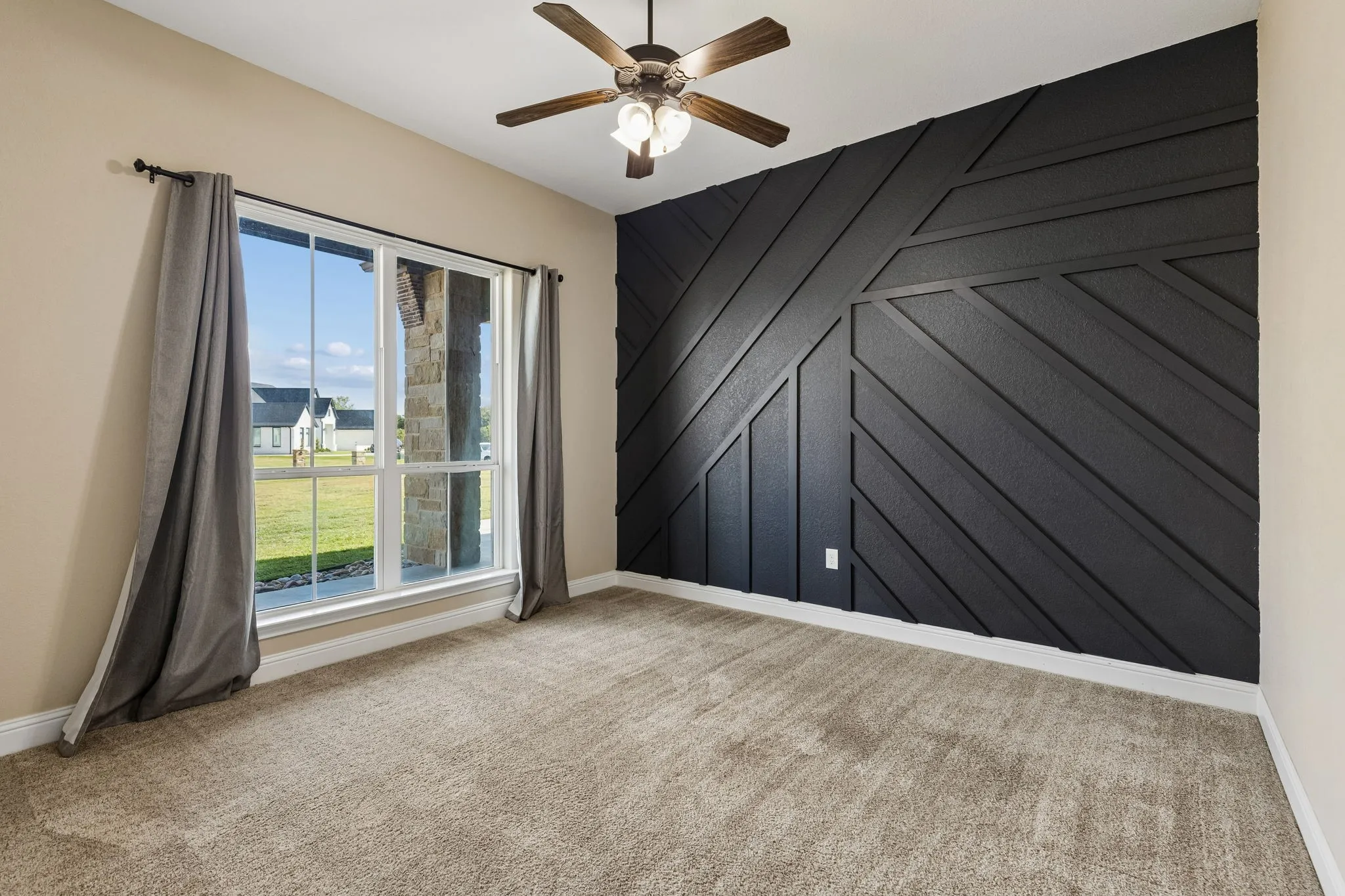 Textured accent wall, ceiling fan with integrated lighting, expansive window, neutral tone carpeting