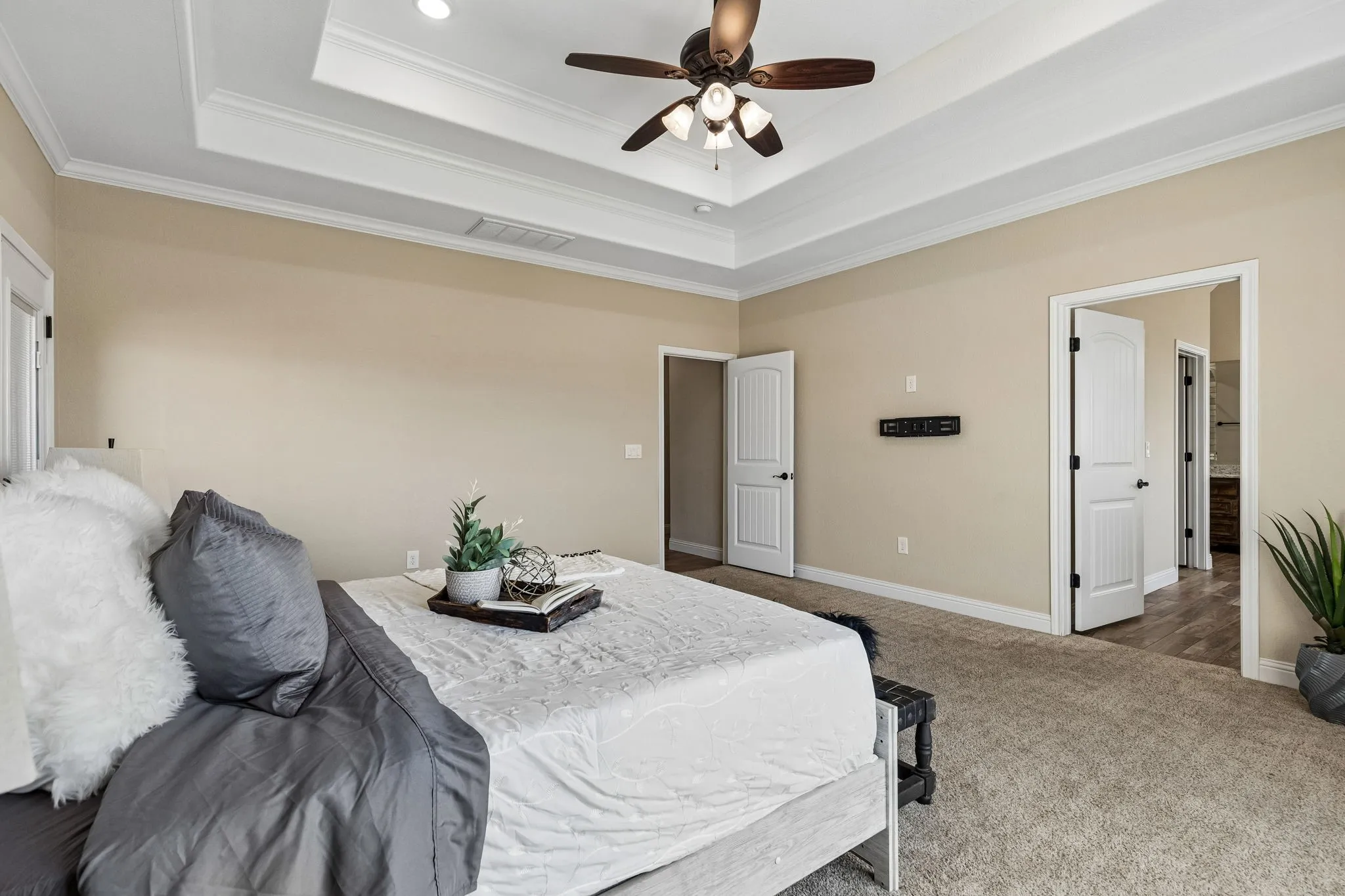Tray ceiling with crown molding, ceiling fan with integrated lighting, carpet flooring, and white interior doors