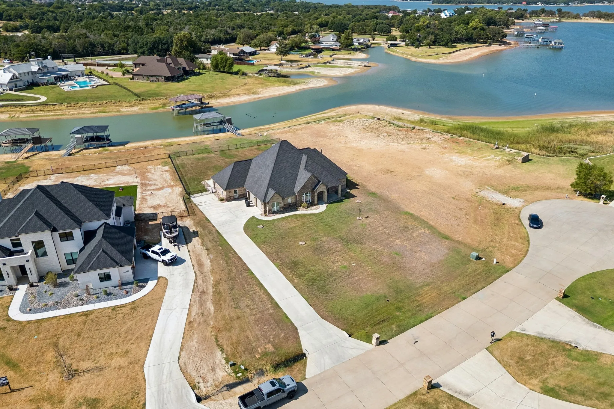 Waterfront property featuring a stone and stucco exterior, dark shingle roofing, and an expansive concrete driveway