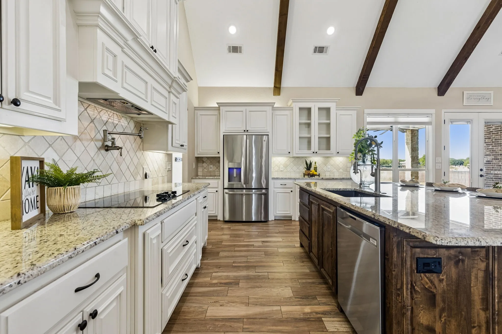 Vaulted ceiling with exposed wood beams, wood-finish flooring, two-tone cabinetry, granite countertops, and stainless steel appliances