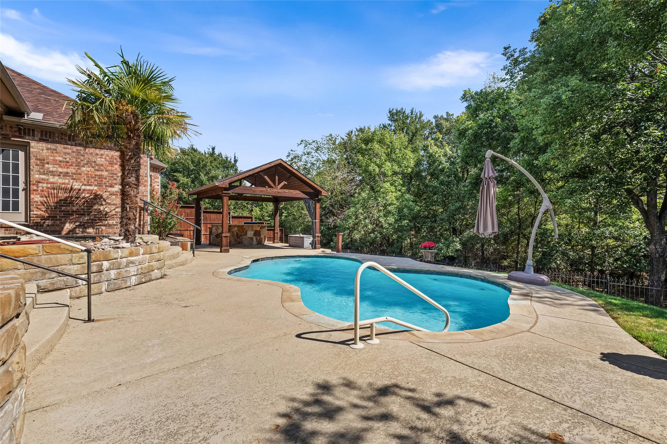 Freeform swimming pool with integrated steps, stone retaining wall, and a wood-beamed gazebo