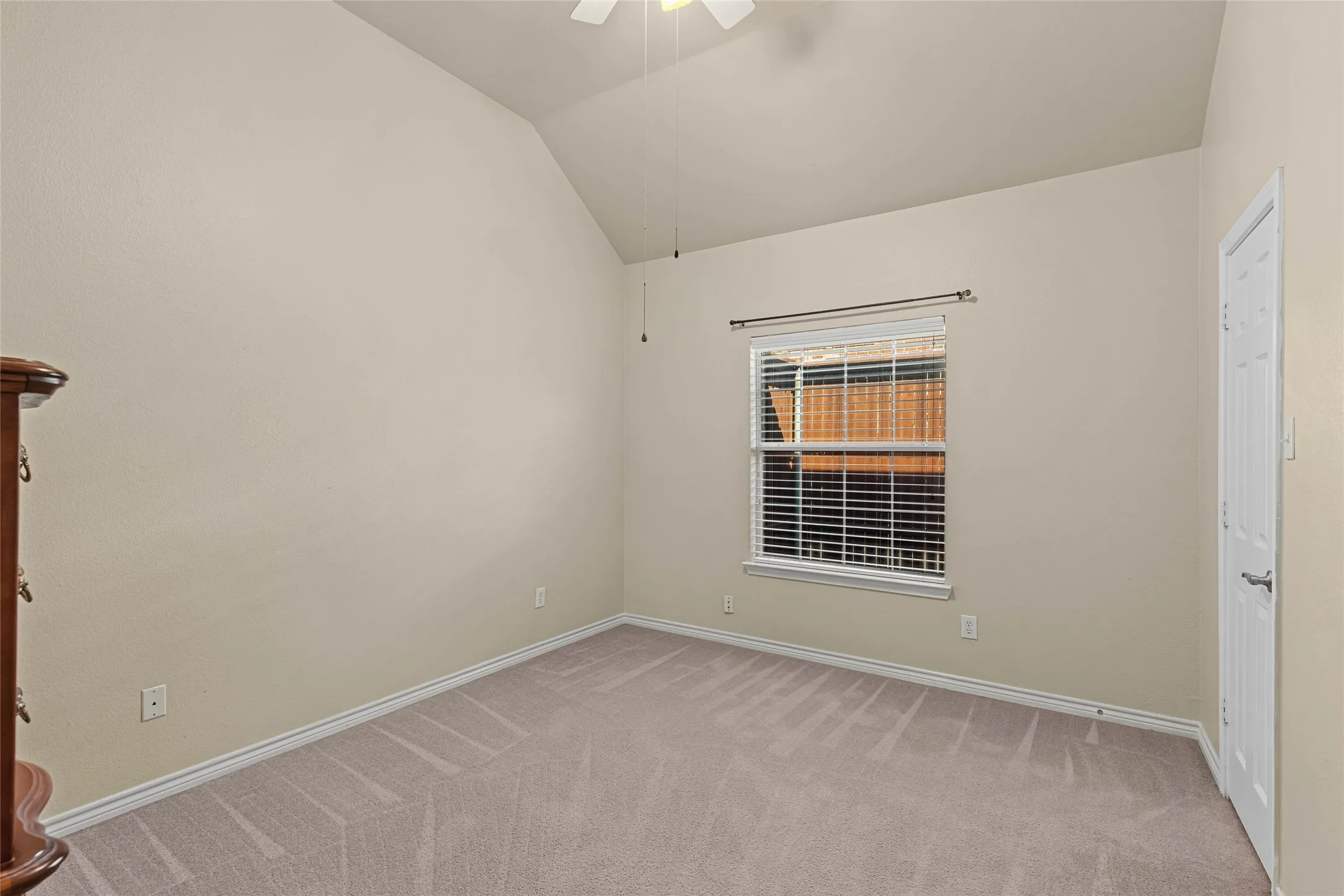Vaulted ceiling, ceiling fan, neutral carpet flooring, window with blinds, and a white paneled door