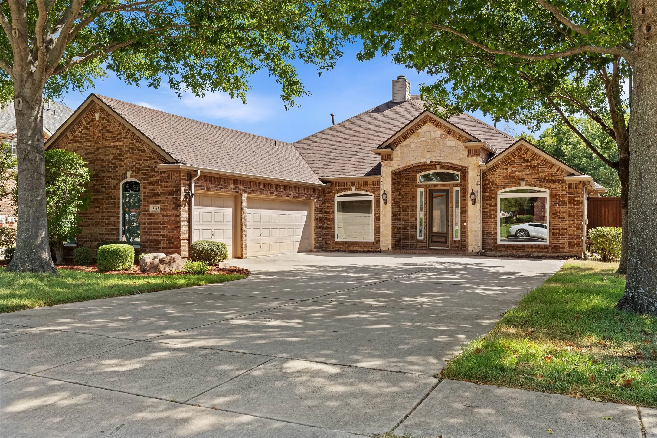 Brick exterior with stone accents, arched entry, two-car garage, and mature trees