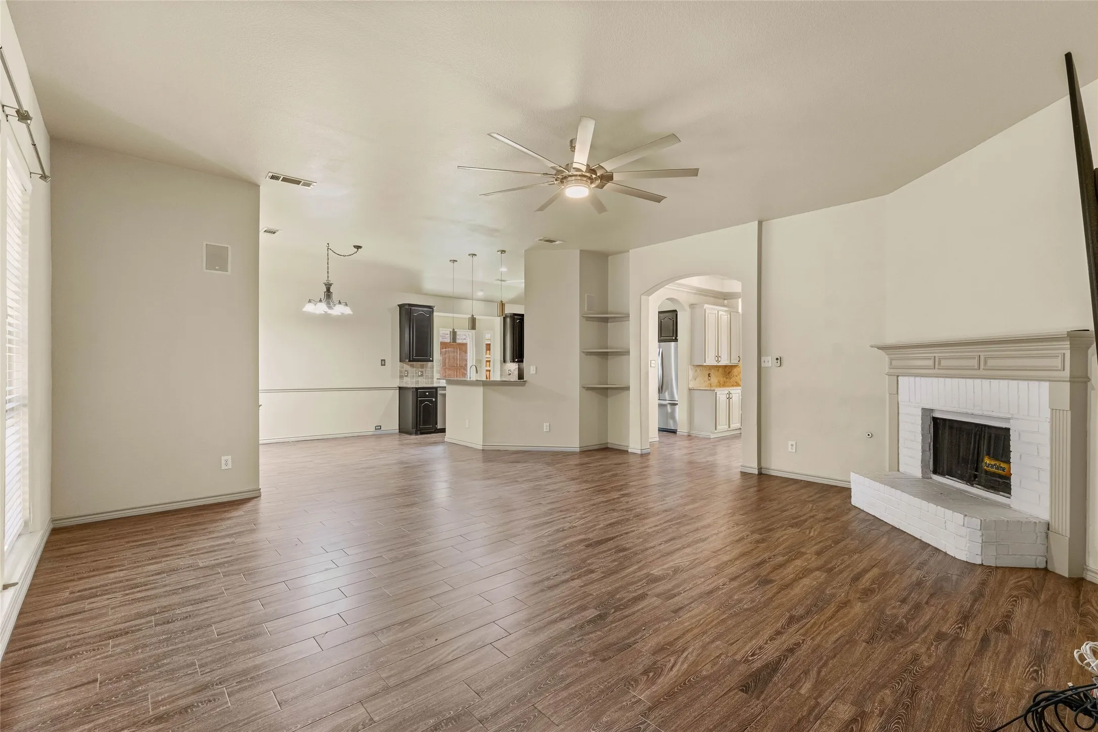 Wood-finish flooring, vaulted ceiling with a ceiling fan, white brick fireplace, arched doorway, and built-in shelving