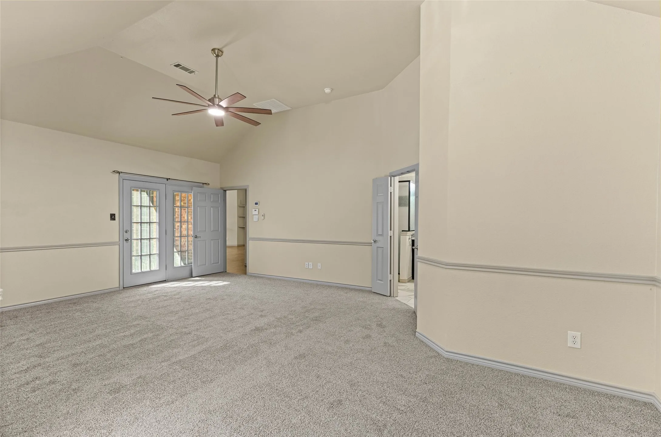Vaulted ceiling with a ceiling fan light fixture, light gray carpeting, and French doors
