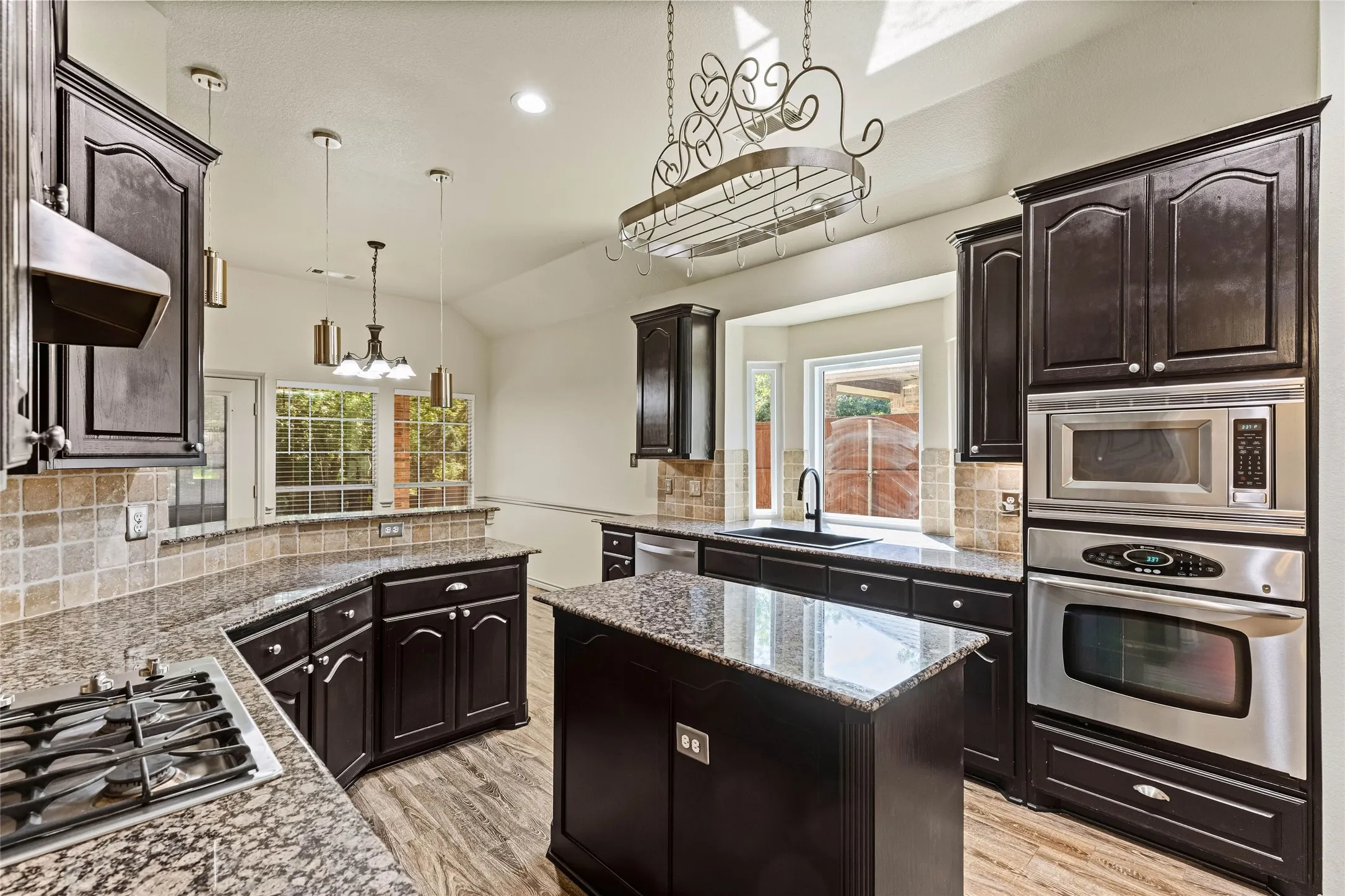 Kitchen featuring dark wood cabinetry, light-toned granite countertops, a tiled backsplash, and stainless steel appliances