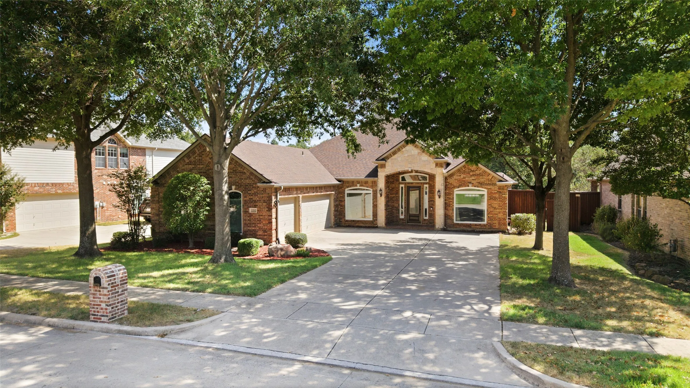 Brick exterior with stone accents, mature trees, and a concrete driveway