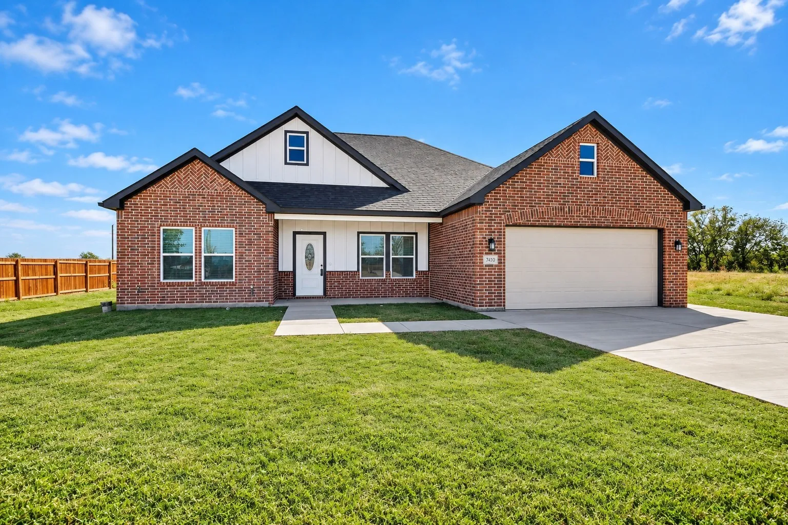 Brick and siding exterior with a dark roof, attached two-car garage, concrete driveway, and a wood privacy fence