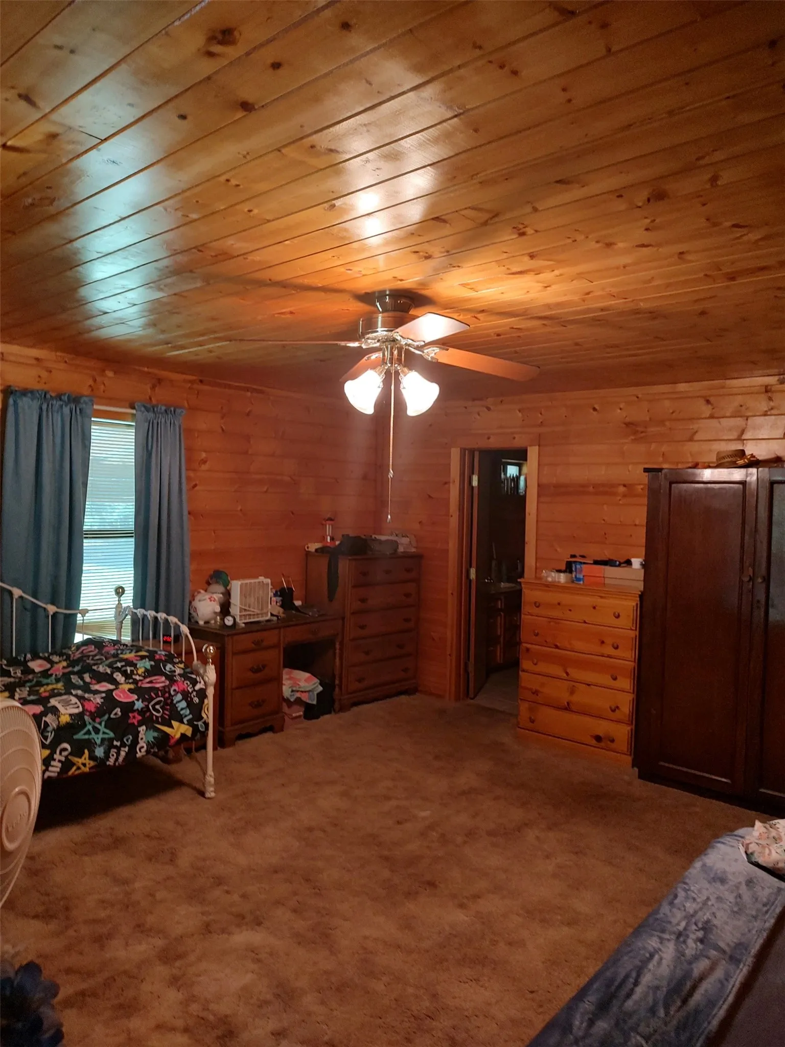 Primary bedroom with wood walls and ceiling, carpet.