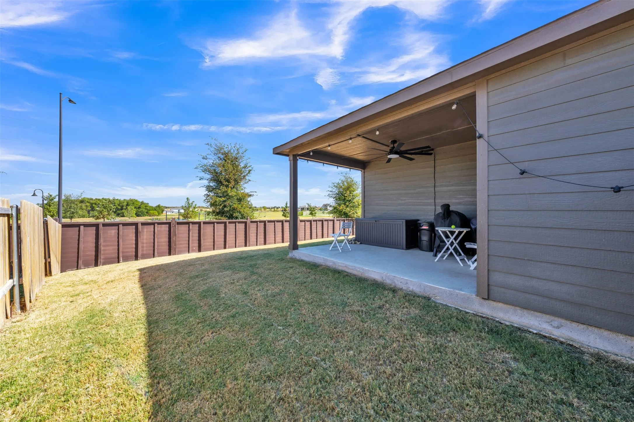Expansive backyard featuring a covered patio, ceiling fan, and string lighting