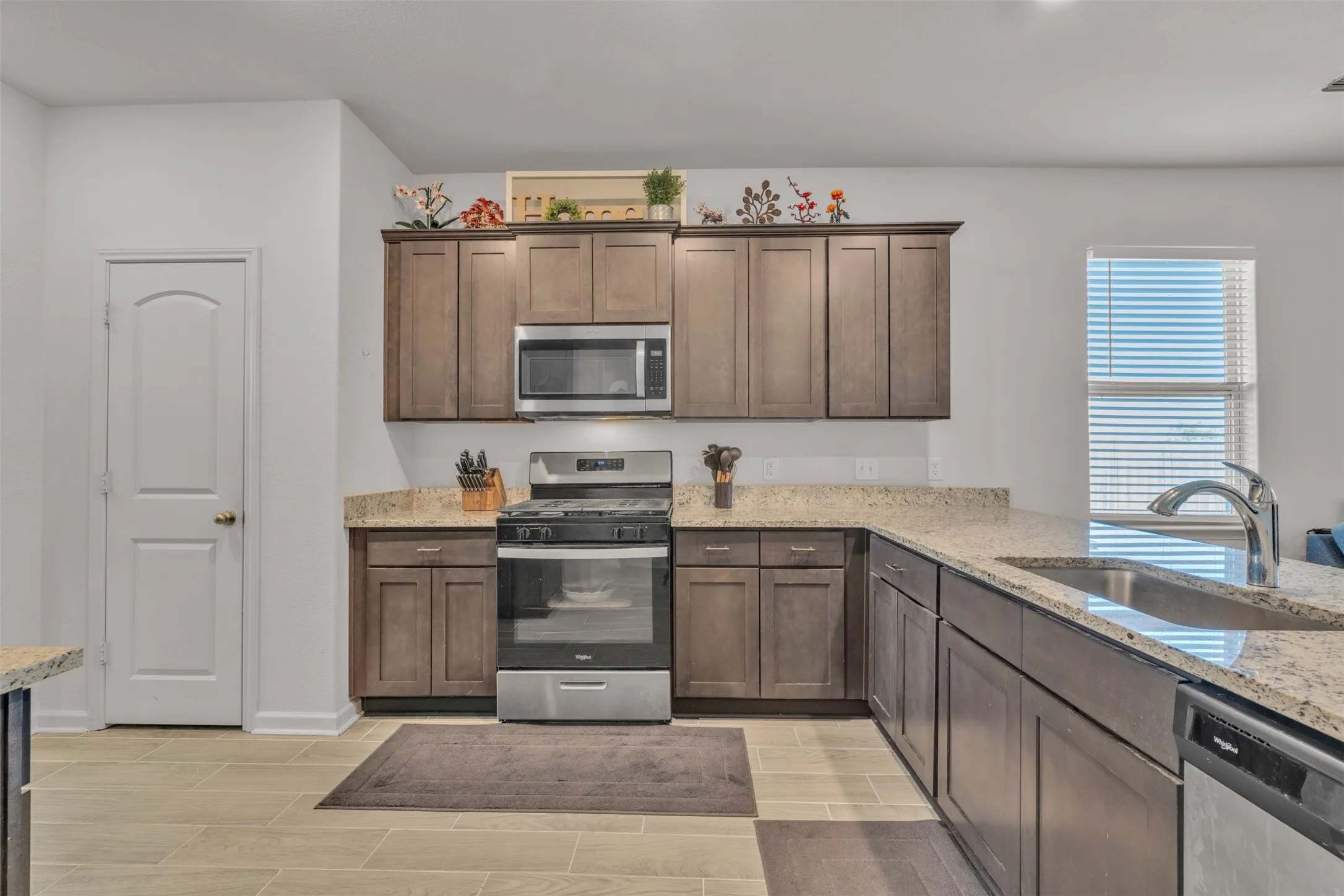 Kitchen featuring wood-finish cabinetry, light-toned countertops, stainless steel appliances, and a stainless steel sink with a gooseneck faucet