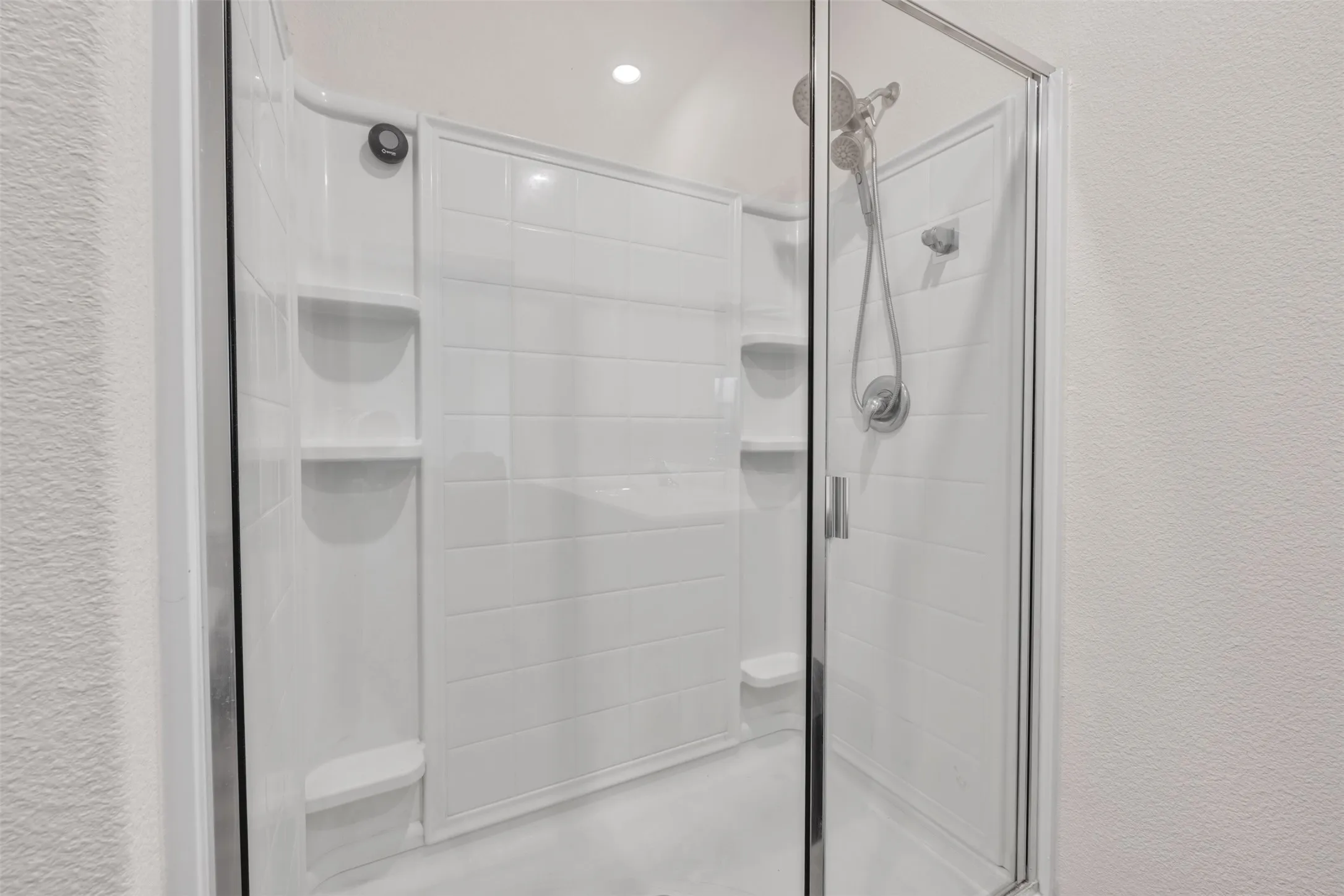 Enclosed shower with a glass door, built-in shelving, and a flexible shower head