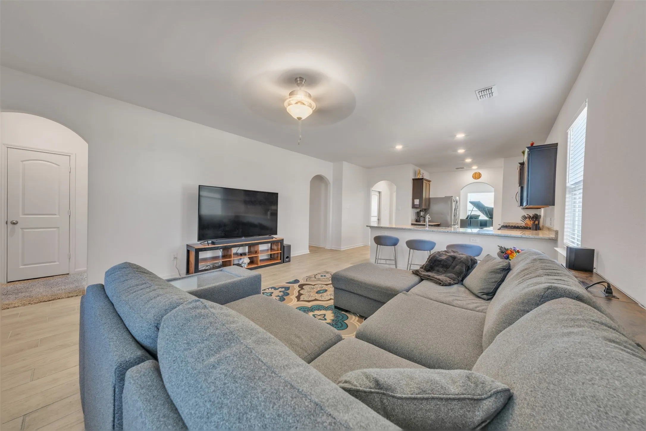 Open concept living space with recessed lighting, light-toned flooring, and a kitchen featuring a breakfast bar with stone-finish countertop and stainless steel appliances