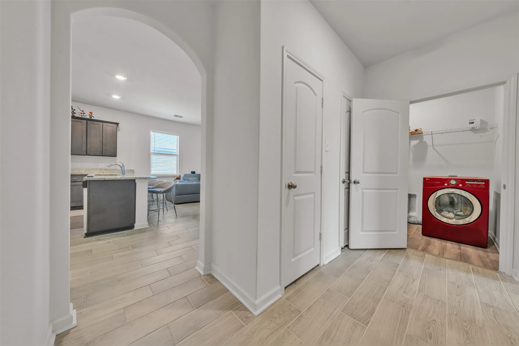 Arched doorway leading to an open-concept area with wood-finish flooring, a laundry closet, and recessed lighting
