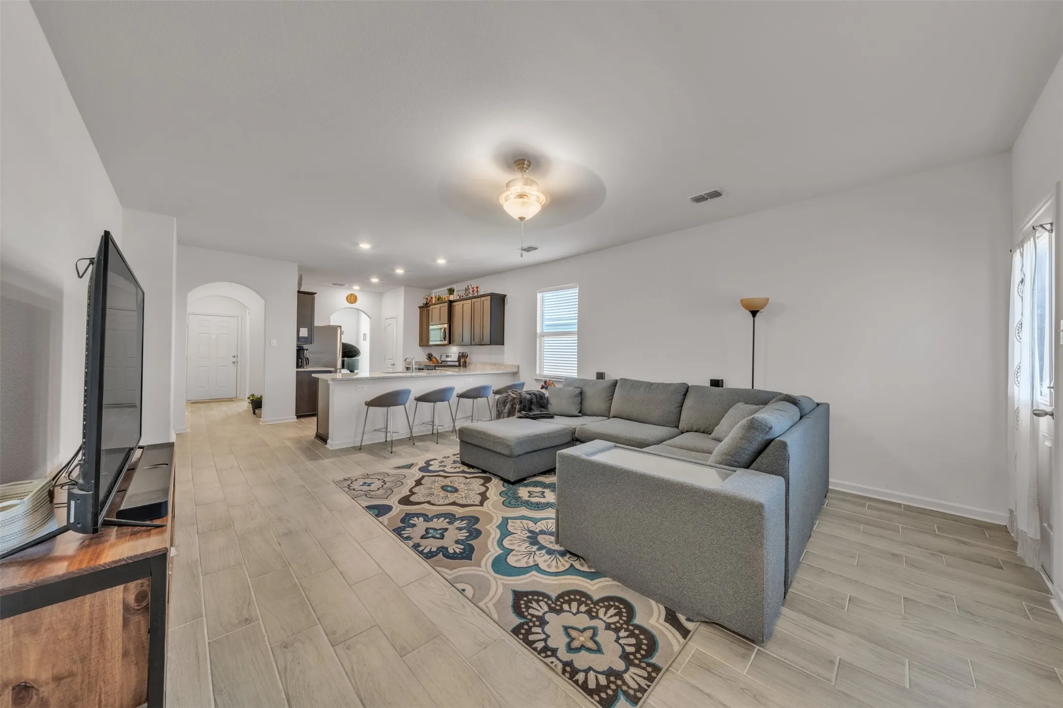 Open-concept living area featuring light-toned wood-finish flooring, a kitchen island with seating, pendant lighting, and recessed lighting