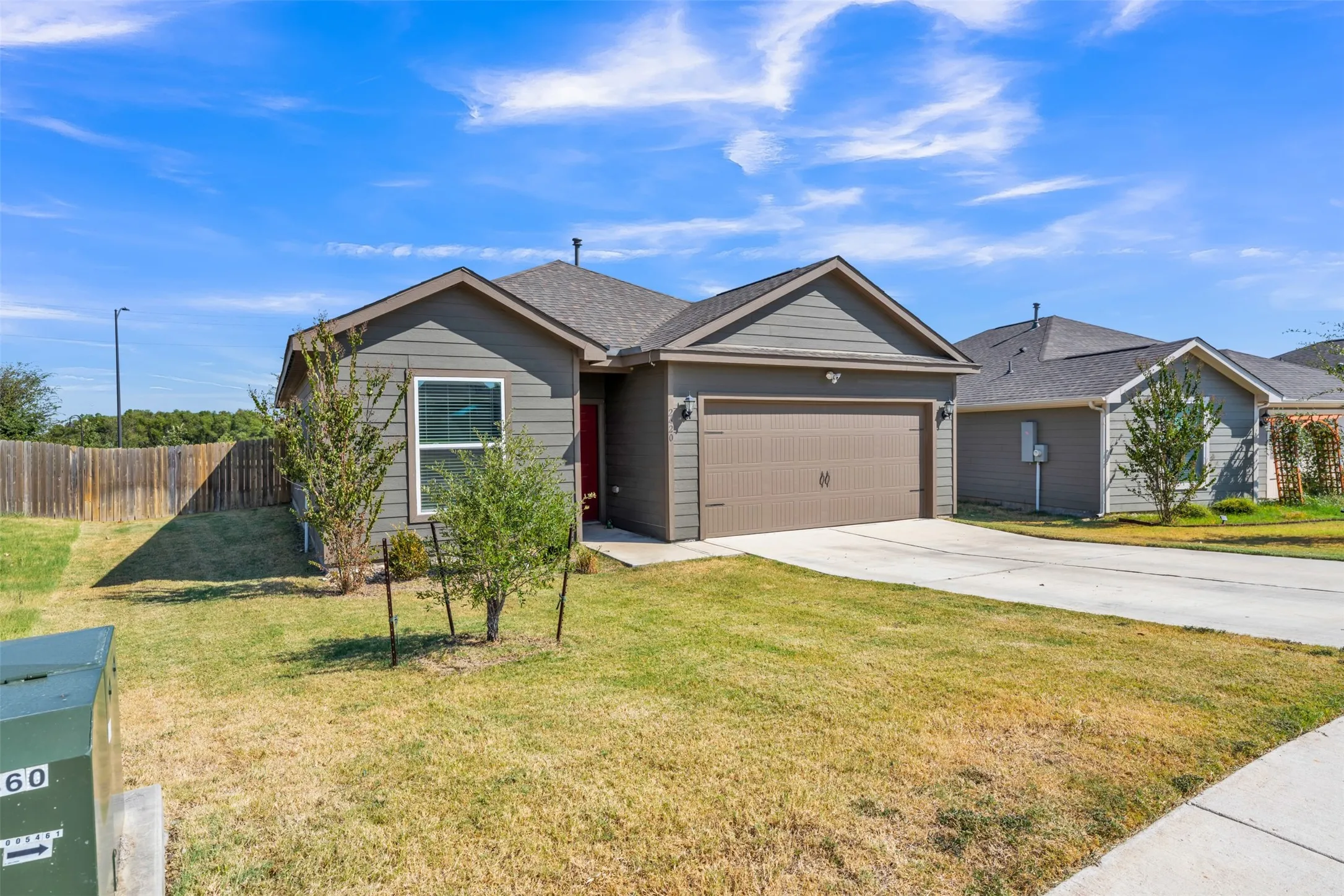 Exterior featuring gray siding, an attached garage, a concrete driveway, a sidewalk, and a fenced perimeter