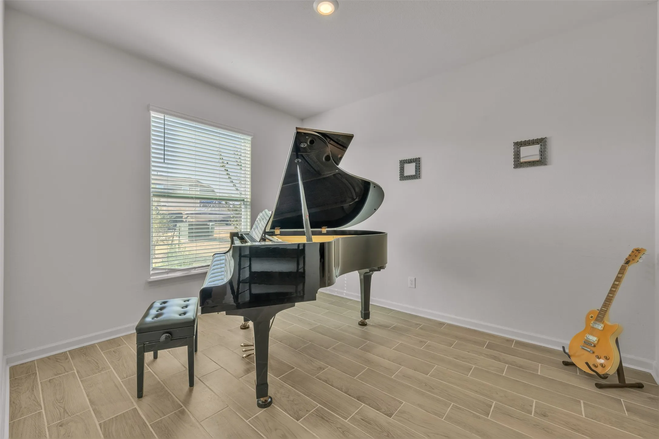 Dedicated music room featuring polished wood-finish flooring, abundant natural light from a large window with plantation shutters, recessed ceiling lighting, and ample space for musical instruments and practice