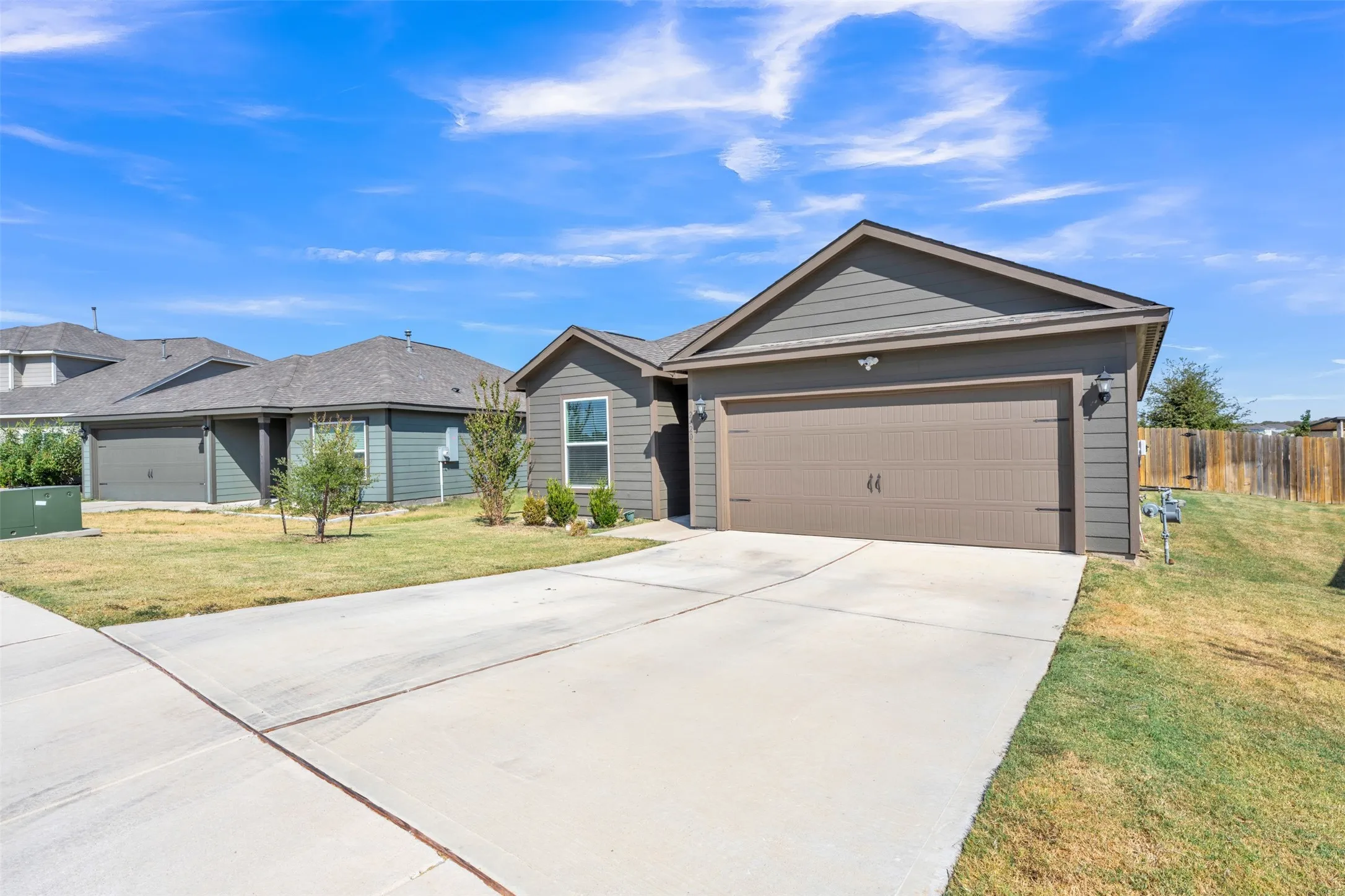 Gable roofline, horizontal siding exterior, attached garage, concrete driveway, and a partially fenced yard