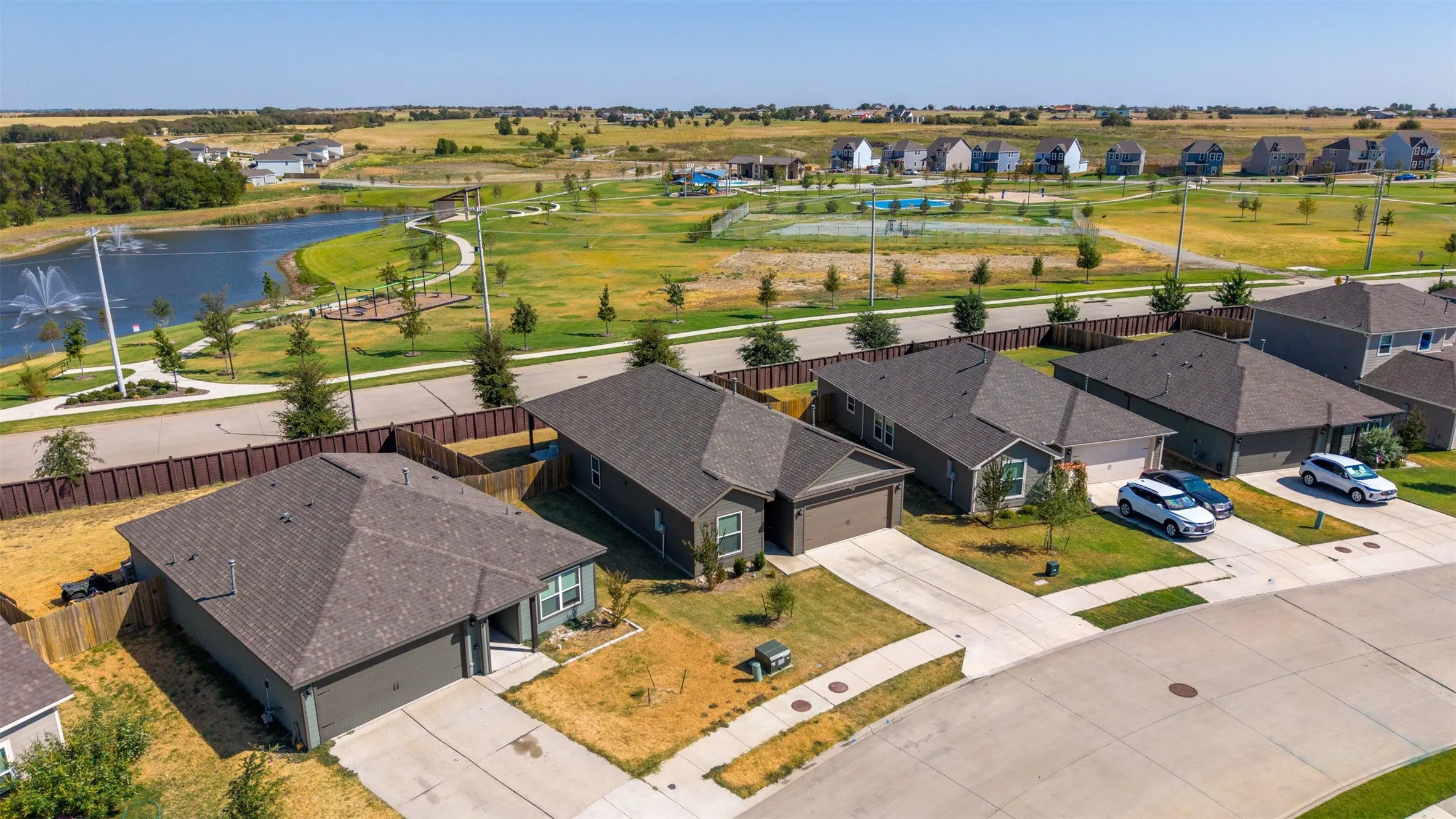 Modern residential community featuring a lake with fountain, paved walking paths, open green spaces, and contemporary single-story homes with attached garages