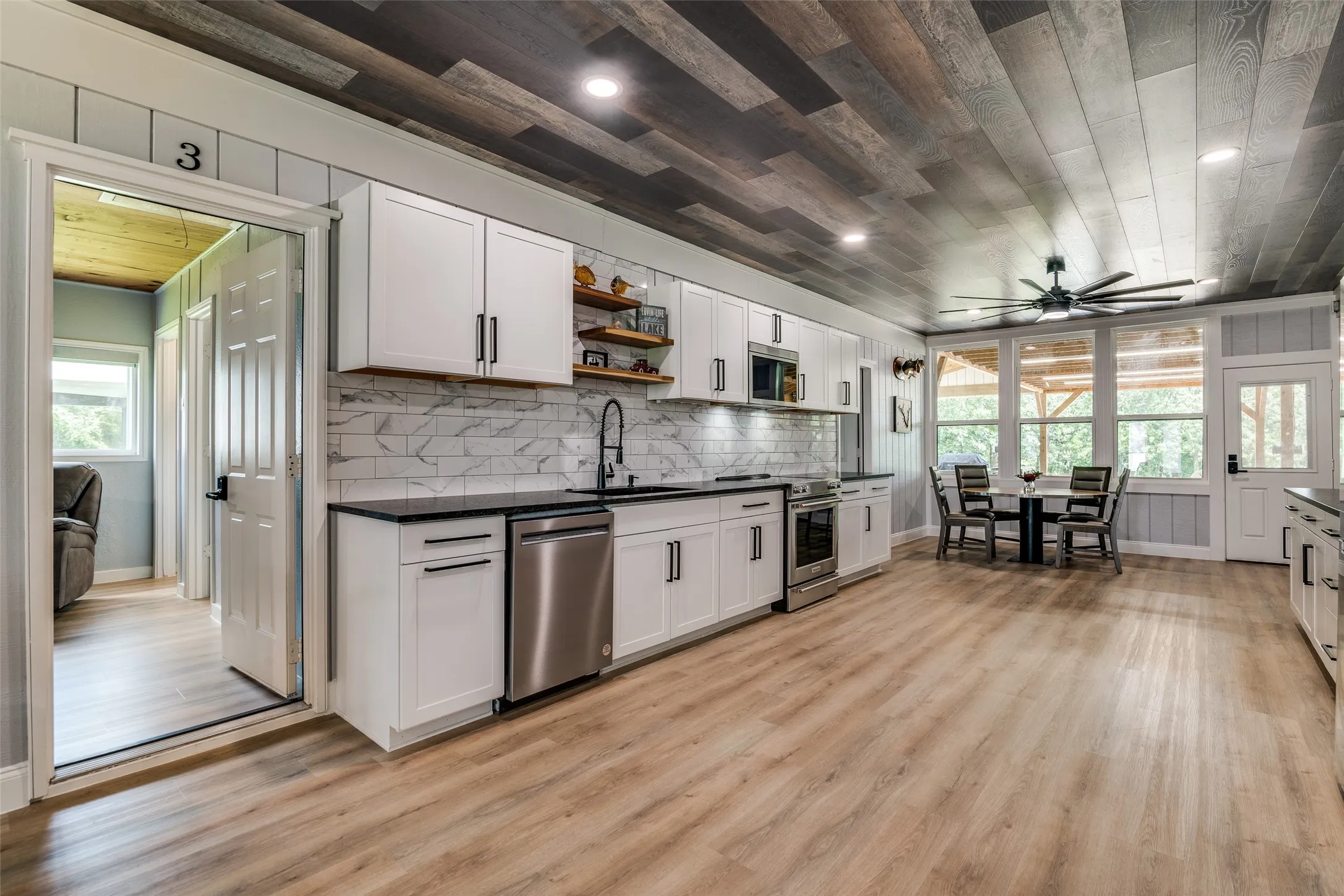 Open-concept kitchen featuring white cabinetry, black countertops, stainless steel appliances, and wood-finish flooring