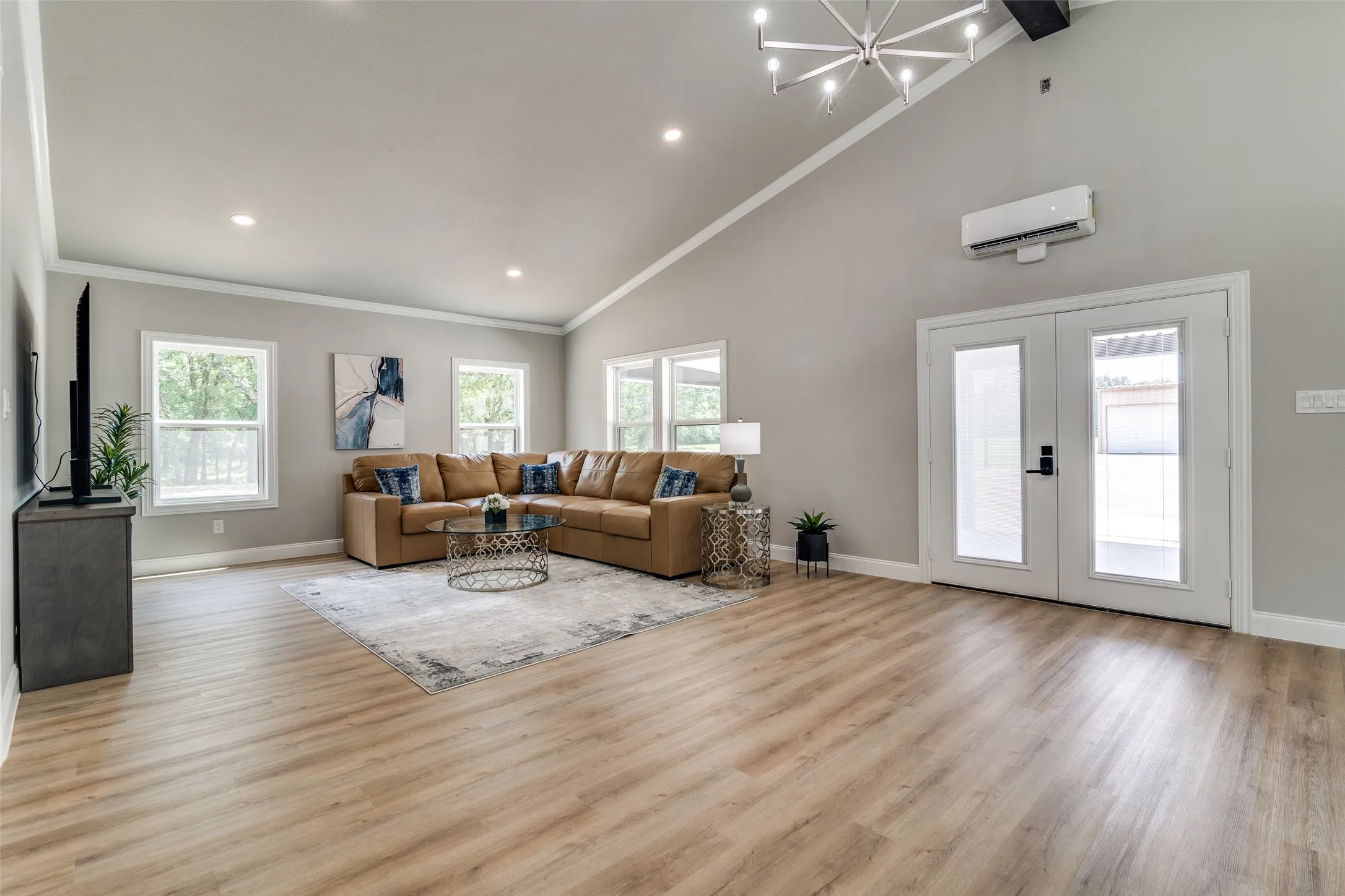 Vaulted ceiling with a contemporary chandelier, multiple windows, double glass panel doors, light wood-finish flooring, and recessed lighting