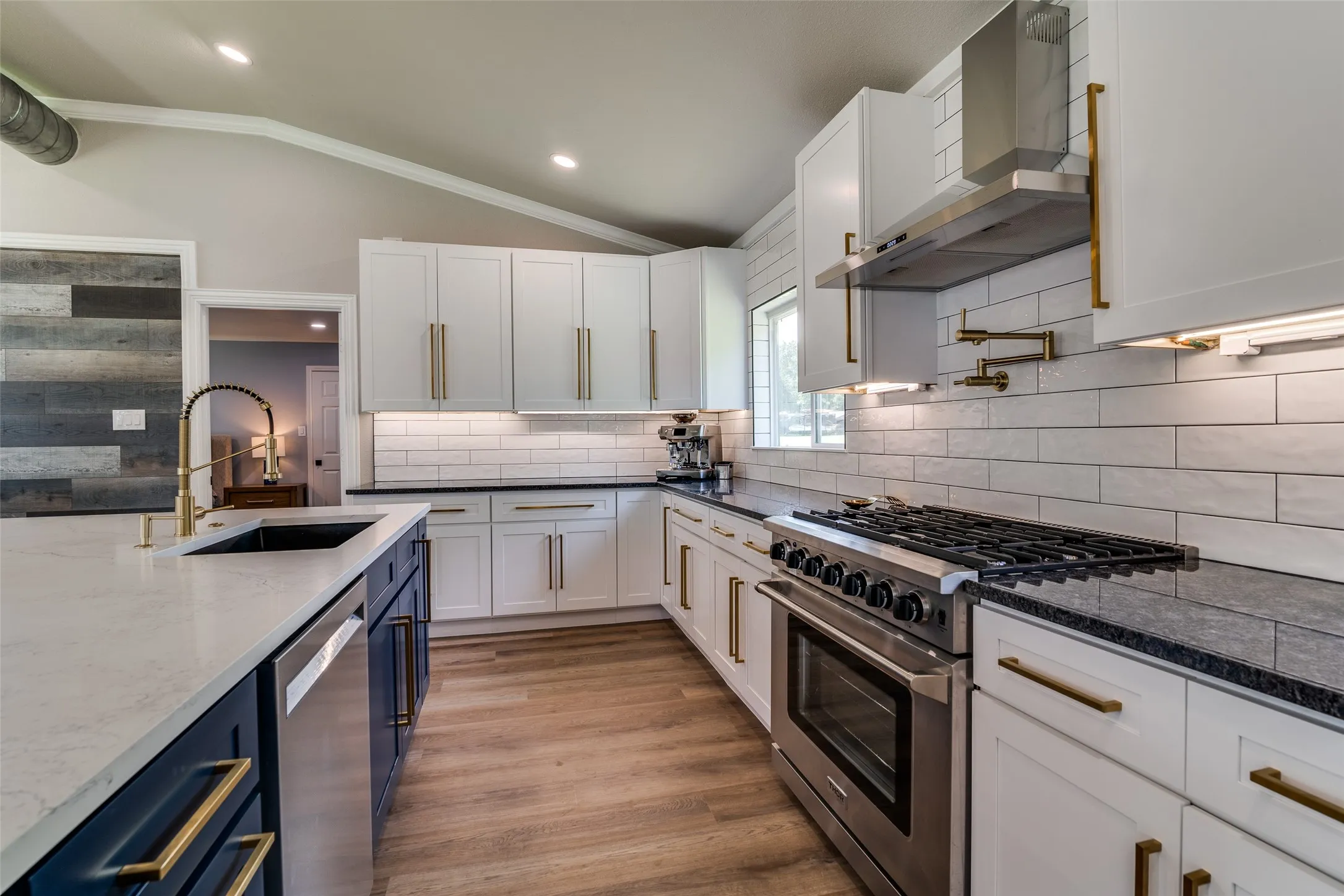 Kitchen featuring white shaker cabinetry, gold-finish hardware, stainless steel appliances, and wood-finish flooring