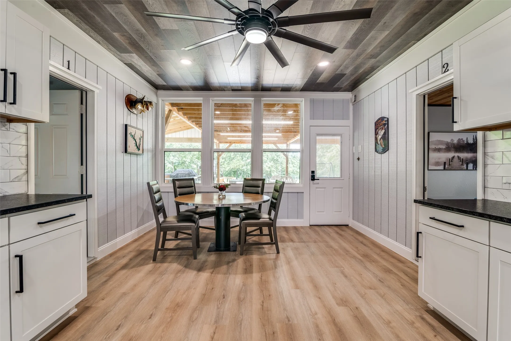 Spacious dining area featuring wood-finish flooring, white shaker cabinetry, dark countertops, and a wood-slat ceiling with a ceiling fan