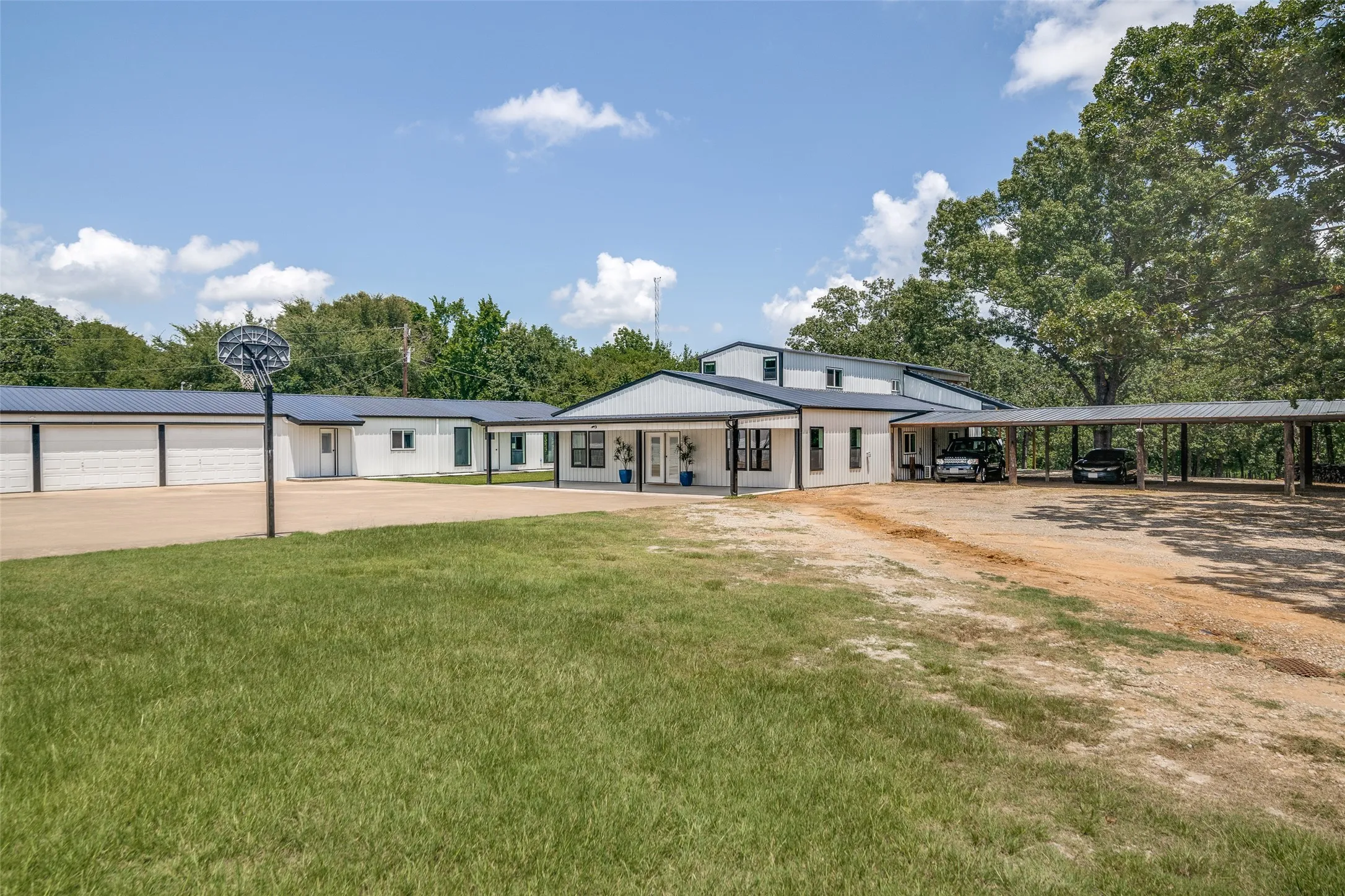 White exterior with black trim, multiple garage bays, an expansive covered carport, and a paved court area