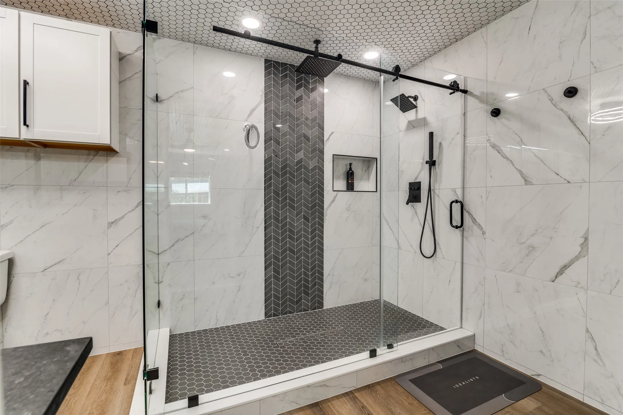 Glass-enclosed shower with a chevron tile accent wall, dual shower heads, and an integrated recessed niche