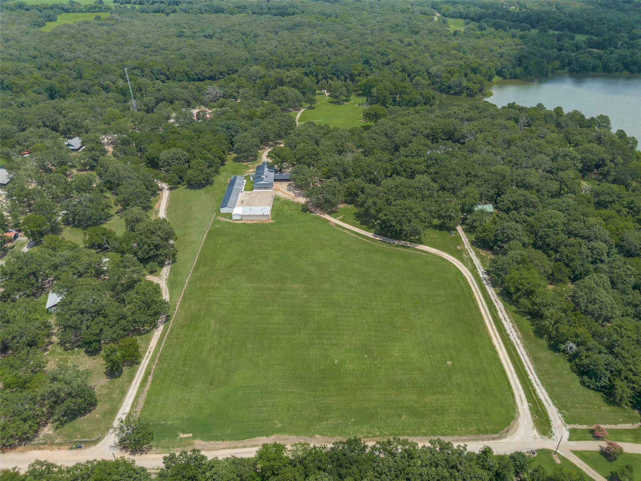 Expansive property featuring a large manicured lawn, multiple structures, and a perimeter of mature trees