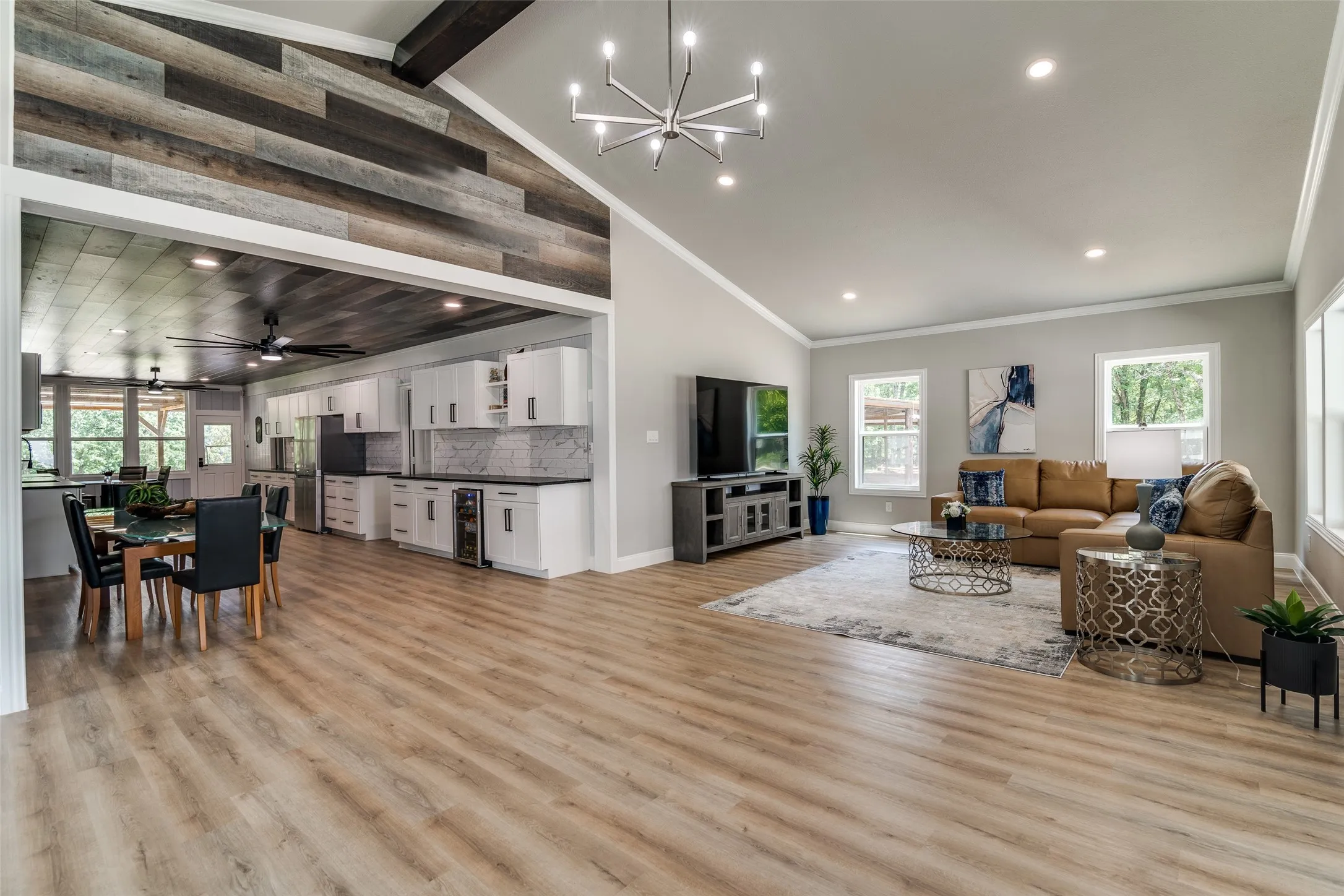Vaulted ceiling with wood-paneled accent wall, wood-finish flooring, recessed lighting, and kitchen with white cabinetry