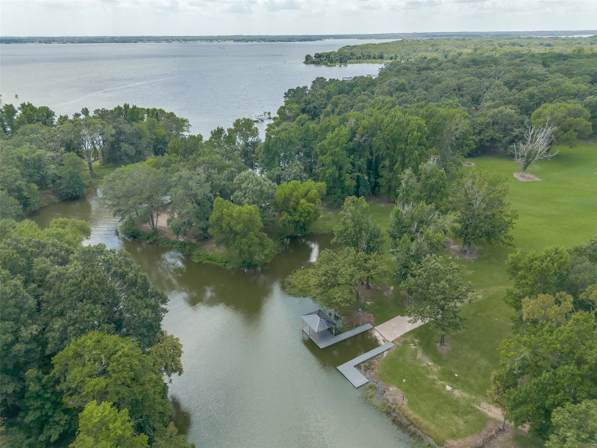 Expansive lakefront property featuring a private boat dock, covered boat slip, concrete boat ramp, and lush tree coverage