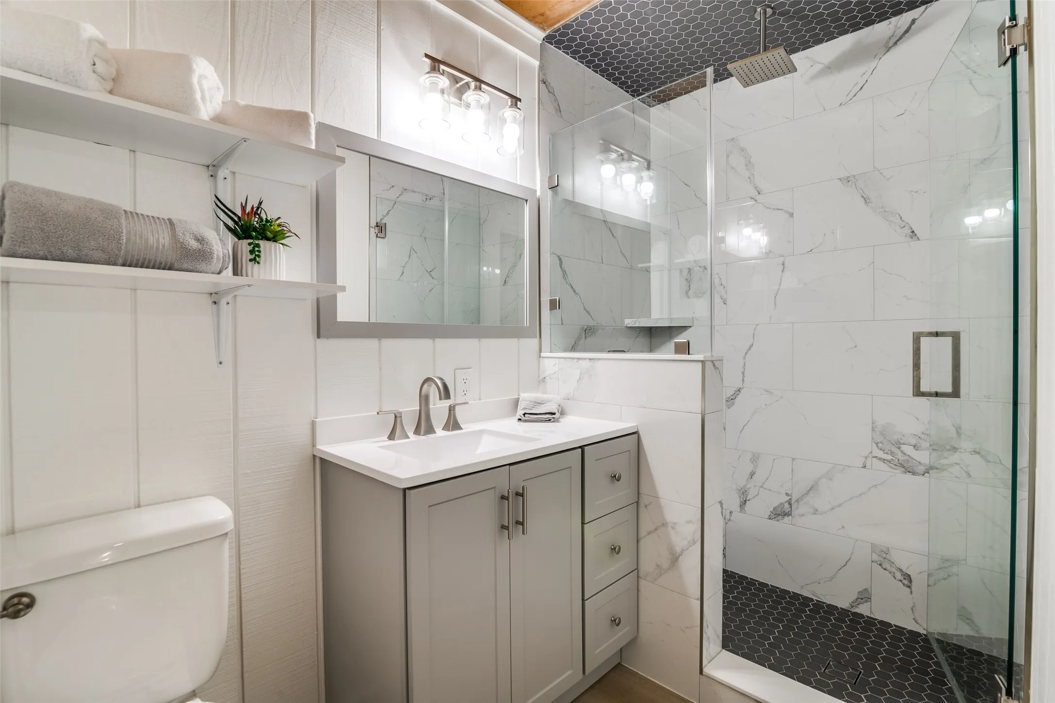 Walk-in shower with floor-to-ceiling tile, dark hexagonal floor tiles, and a rainfall showerhead
