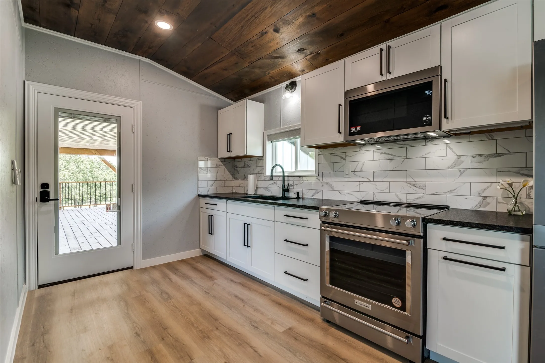 Wood-finish flooring with white shaker-style cabinetry, black countertops, and a white subway tile backsplash