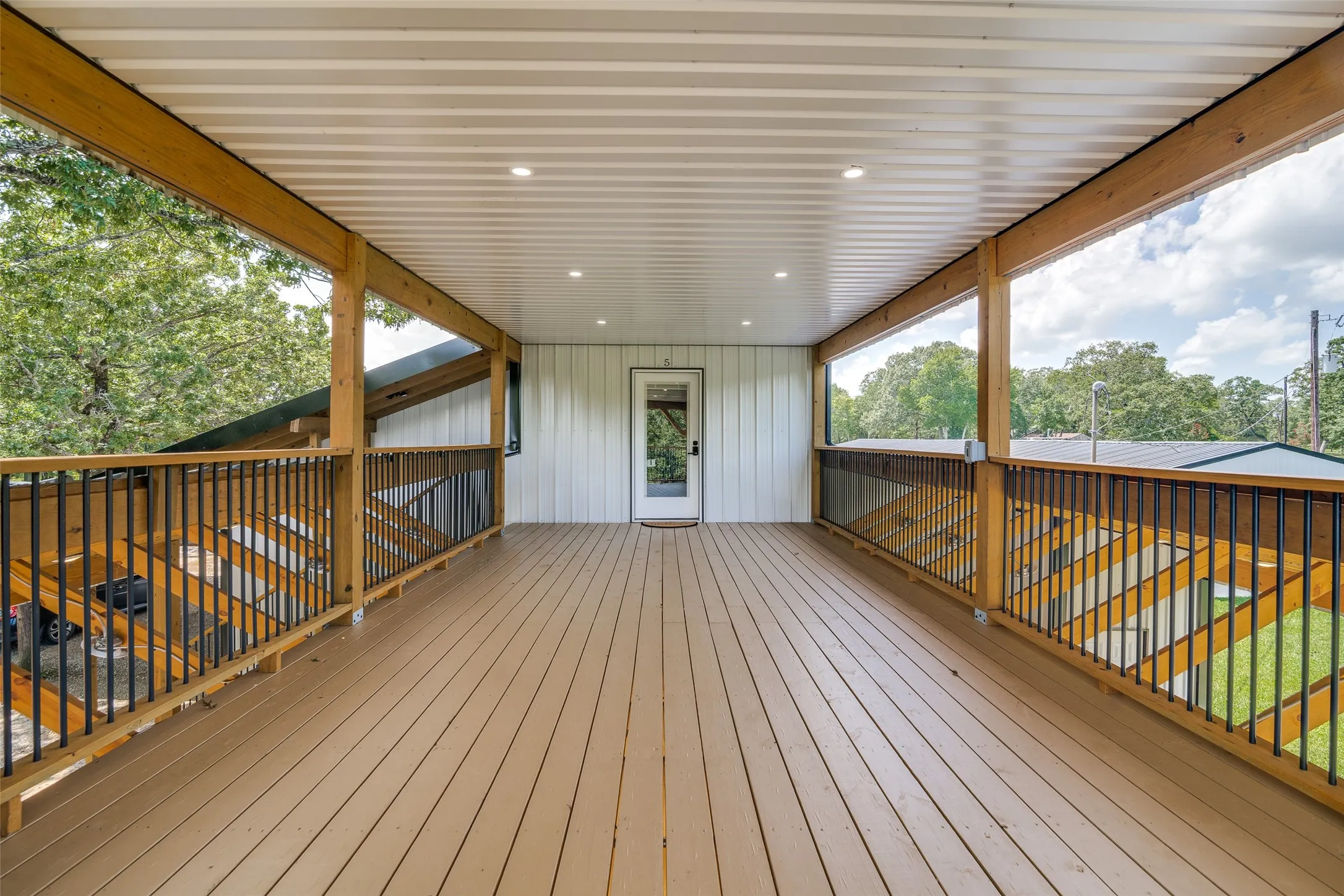 Expansive covered deck featuring wood-finish flooring, recessed lighting, and black metal railings with wood posts