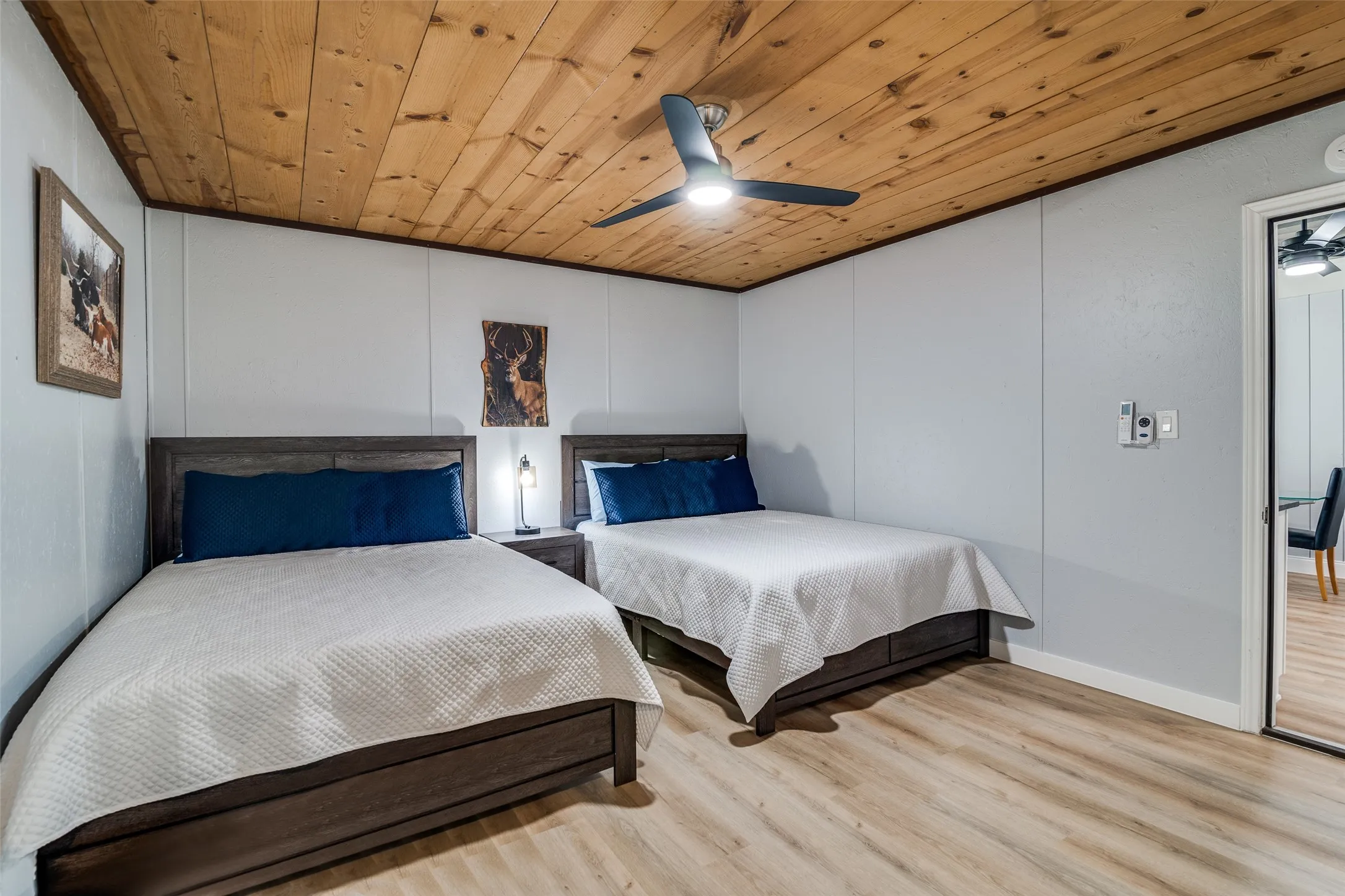 Wood-finish flooring with a natural wood plank ceiling, light gray panel walls, and a ceiling fan with integrated lighting