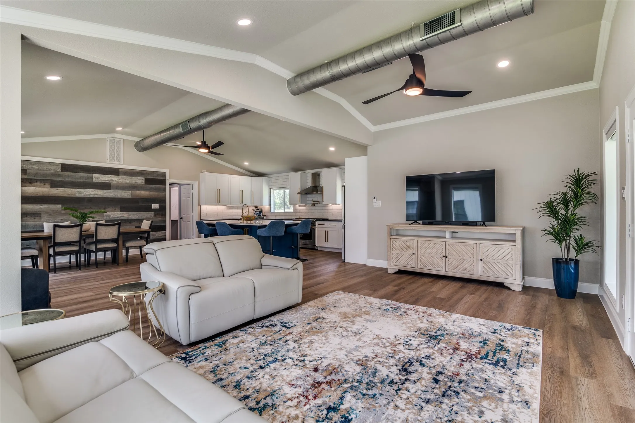 Vaulted ceilings with exposed ductwork, wood-finish flooring, recessed lighting, and a dining area with a wood accent wall