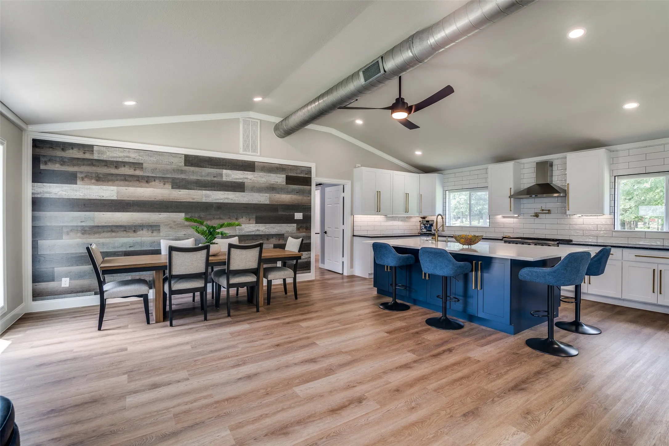 Vaulted ceilings, wood-finish flooring, accent wall, kitchen island, and stainless steel range hood