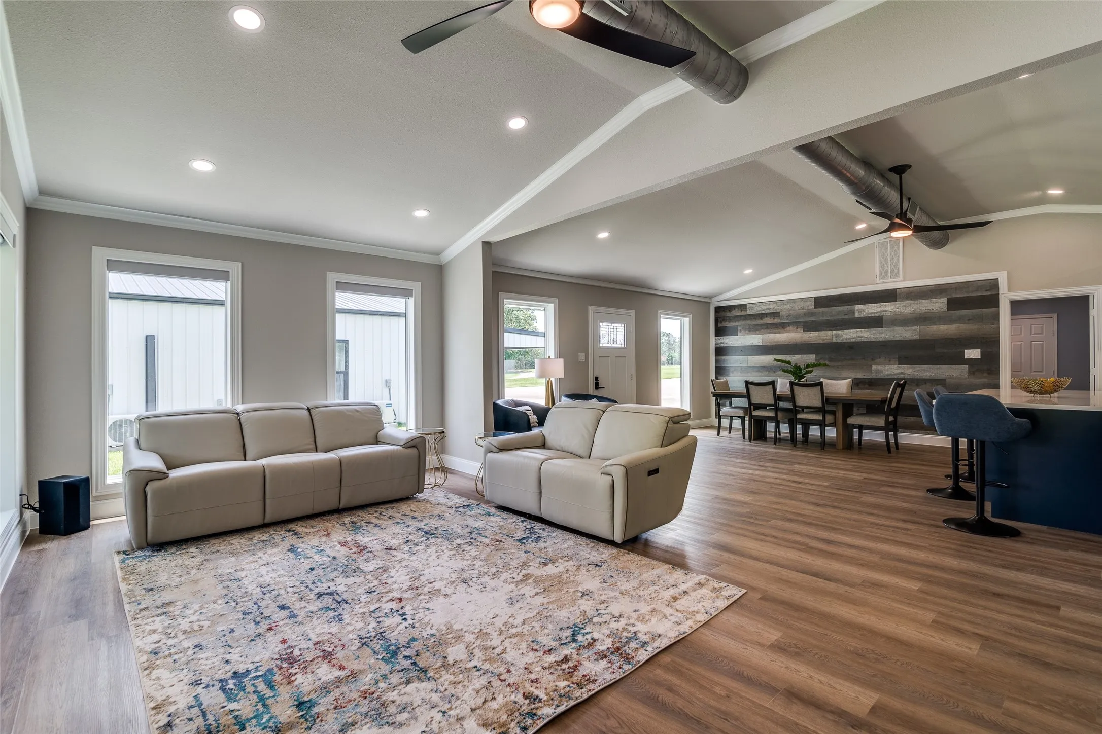 Open-concept living space featuring vaulted ceilings, recessed lighting, wood-finish flooring, a decorative accent wall, and exposed ductwork