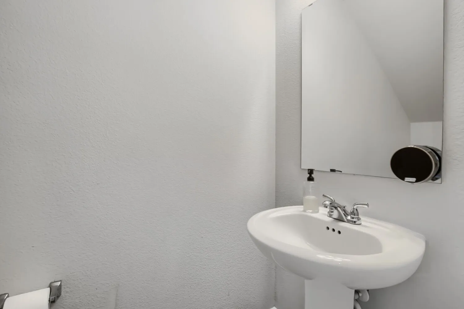 White ceramic pedestal sink with a chrome-finish faucet and an unframed wall mirror