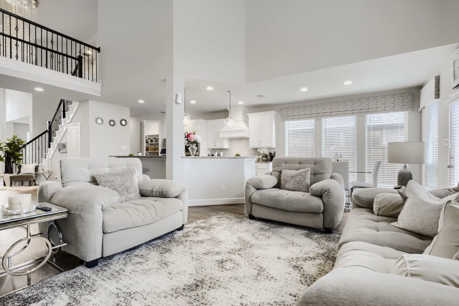 Spacious open-concept living area featuring a double-height ceiling, recessed lighting, wood-finish flooring, a kitchen island, and multiple windows