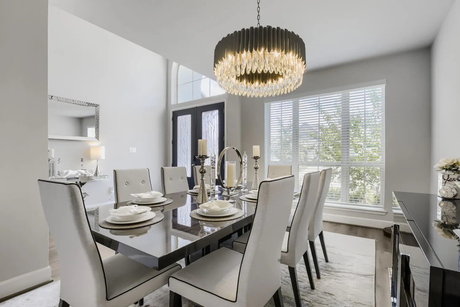 Formal dining area featuring a high ceiling, wood-finish flooring, a contemporary chandelier with crystal accents, and large windows with blinds