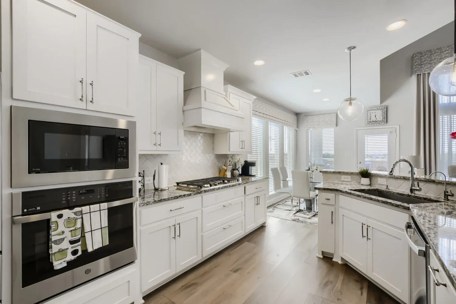White shaker cabinetry, stainless steel built-in appliances, wood-finish flooring, stone countertops, and a tile backsplash