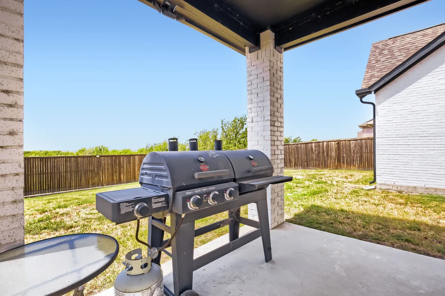 Covered patio with a concrete slab, brick support column, and a wood privacy fence