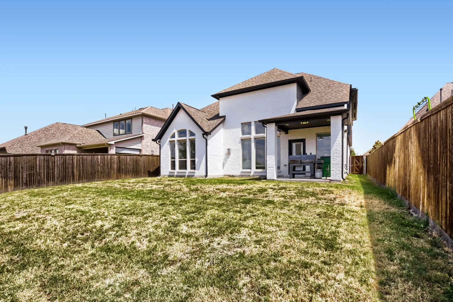 Rear exterior with white brick facade, arched window, covered patio, and wood privacy fencing