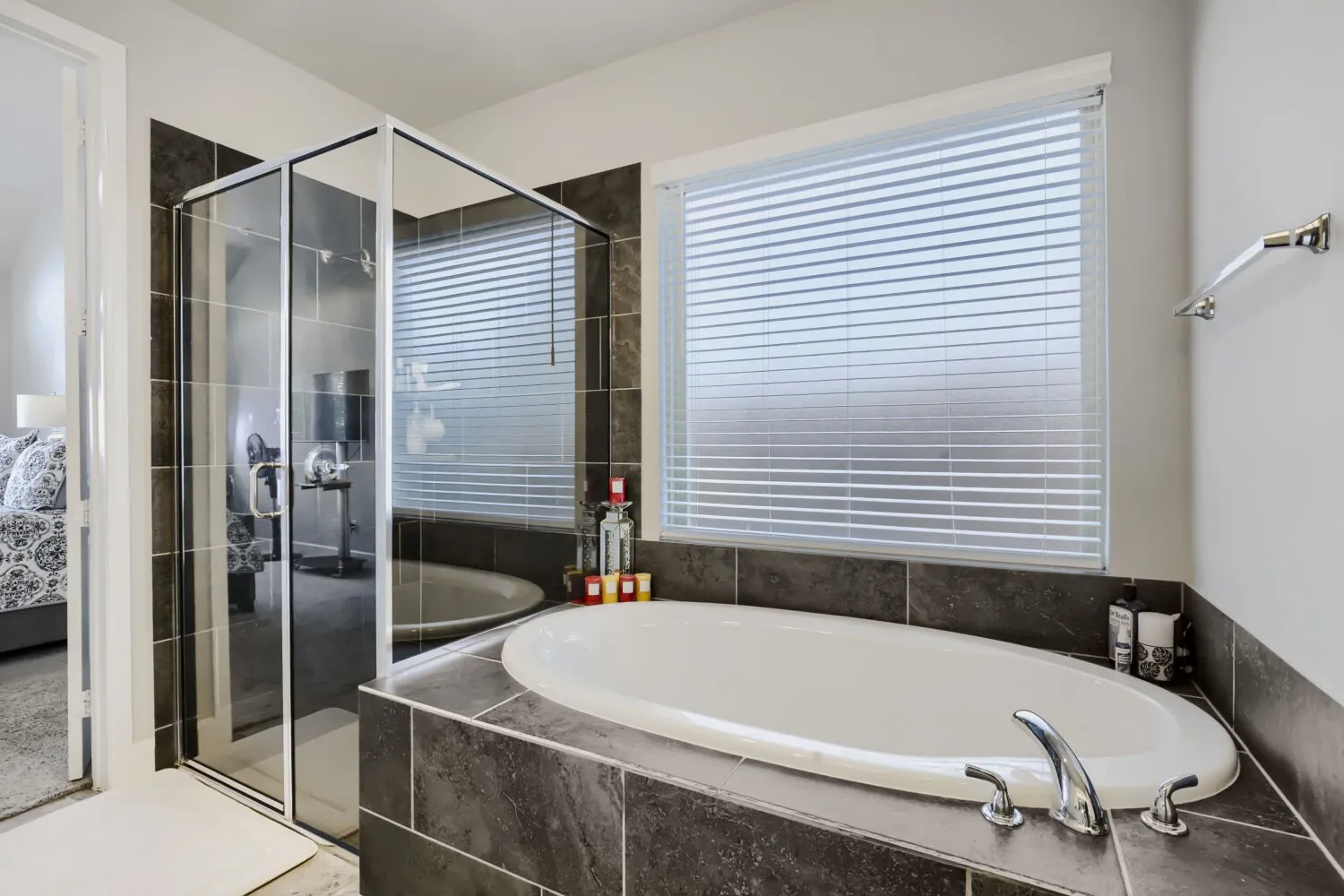 Soaking tub with deck-mounted chrome fixtures, glass-enclosed shower, and tiled surround