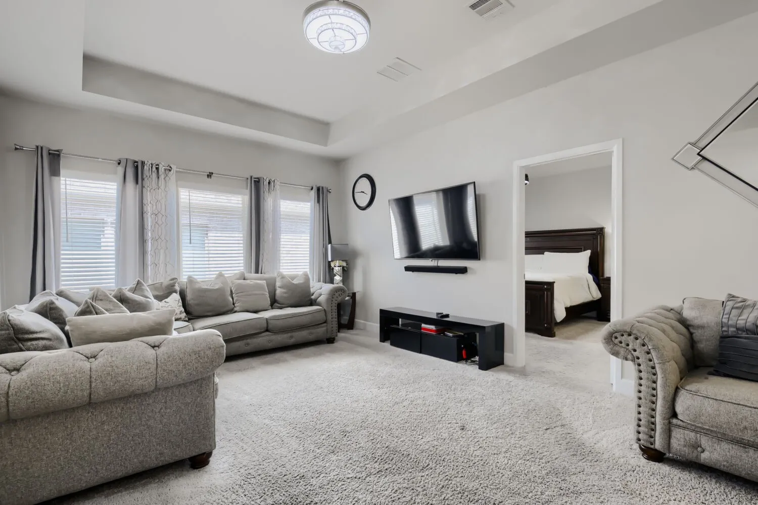 Recessed ceiling, flush mount chandelier, wall-mounted television, and light-colored carpeting