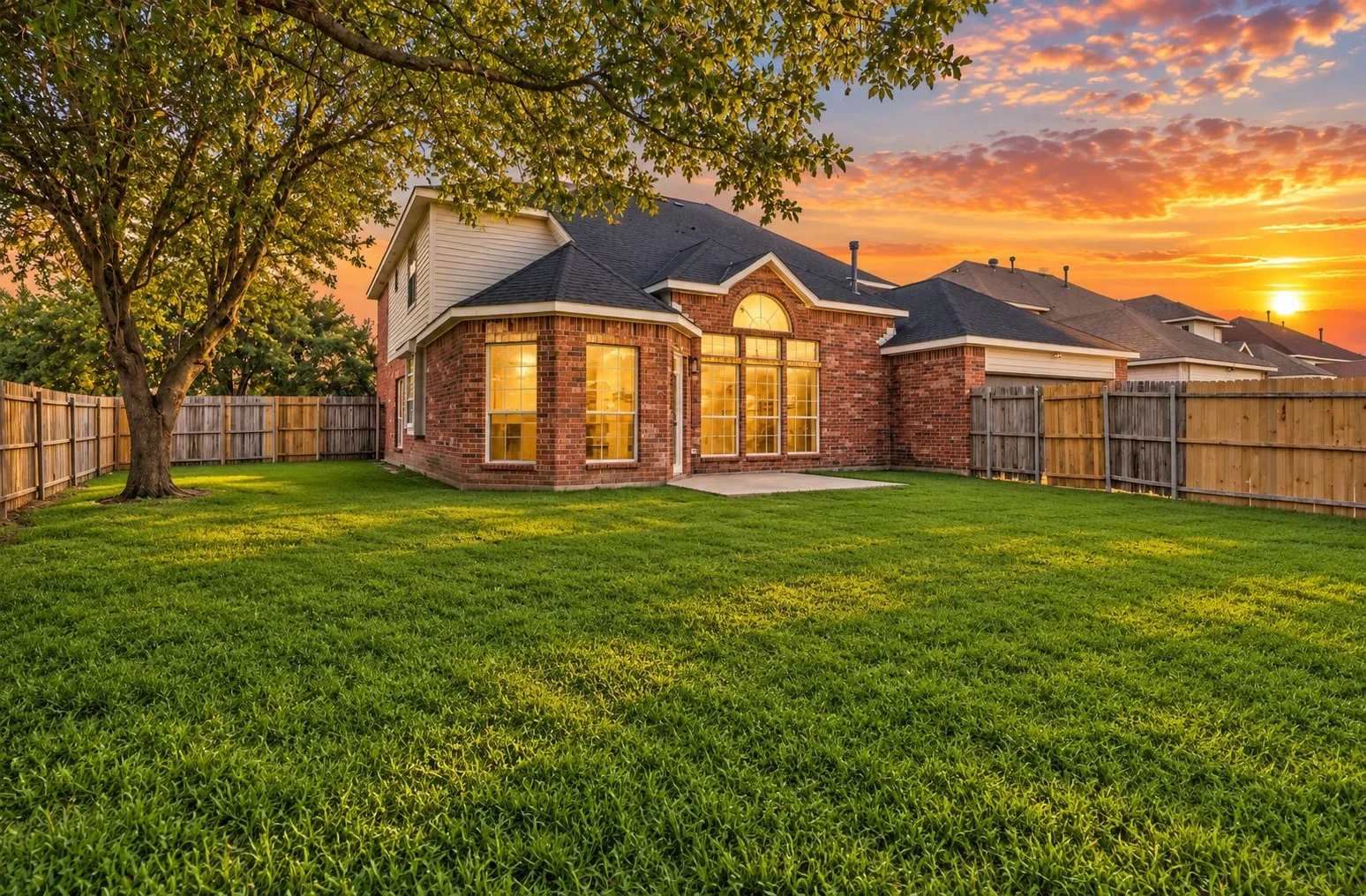 Expansive backyard featuring a large green lawn, mature tree, wood privacy fencing, and a concrete patio